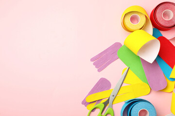Scissors, bright kinesio tape rolls and pieces on pink background, flat lay. Space for text