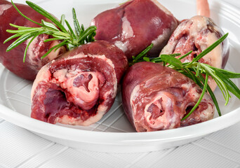 Raw turkey hearts with rosemary sprigs on white plate.