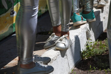 Close-up of the legs of teenagers in sports shoes and silver leggings standing by the fence on the...