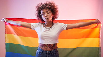 lgbtq concept. Positive caucasian girl with afro curly hair holding rainbow flag isolated in studio