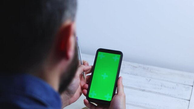 Man at home using Smartphone with Green Mock-up Screen, doing swiping, screen has tracking Markers