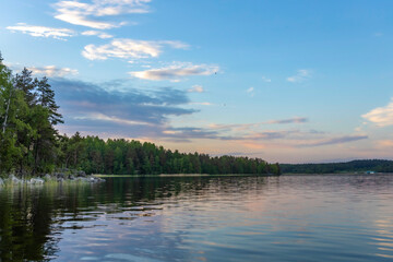 Evening landscape with a sunset sky on the lake. Clouds and forest are reflected in the water. Ducks fly over the lake.