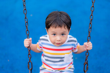 Little asian boy on a swing in summer garden on warm and sunny day outdoors., Background. Copy space.