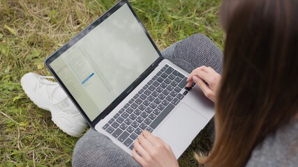 Top view Girl working on laptop on the street sitting on the grass. Girl Student or Freelancer...