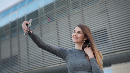 Close up of the young caucasian woman having a video chat on the modern building background. Outdoors. POV of the charming and happy girl. Close-up Of A Beautiful Sports Girl Holding A Smartphone