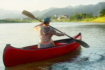 Woman rowing oars while floating on kayak on river against background of houses in countryside.