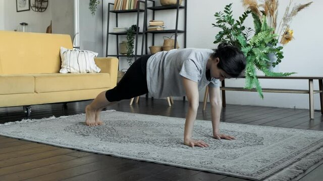 Strong fit young woman is practising plank position at home developing stamina and strength during individual practice at home. House, youth and sports concept.