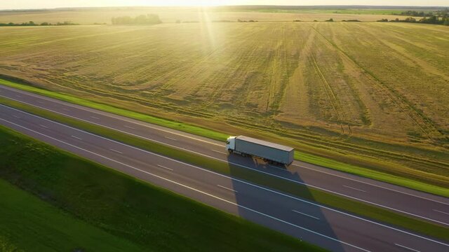Aerial shot: vehicles, trucks and cars driving by road. Sunset summer time.