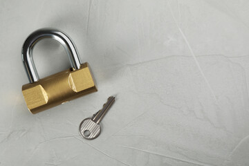 Modern padlock with key on light grey table, flat lay. Space for text