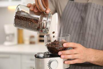 Man using electric coffee grinder in kitchen, closeup - Powered by Adobe