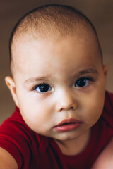 Portrait of cute baby close-up. Sweet little infant looks to camera. Bald baby with brown eyes and long lashes