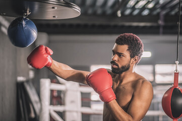 African american kickboxer having a workout in a gym and kicking the sandbag