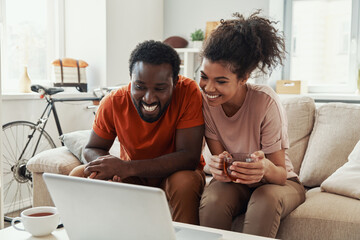 Beautiful young African couple looking at laptop and smiling while spending time at home