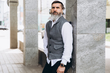 Obraz premium Bearded gray-haired senior man listening to music on the clean urban spaces