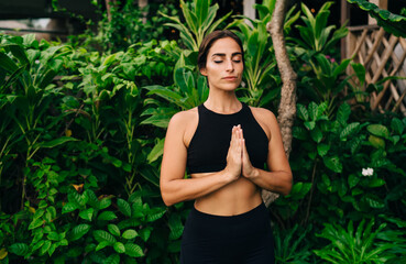 Beautiful female yogi in black sportswear practice hatha during morning meditation on nature, attractive woman in namaste pose getting inner peace and feel soul harmony keeping healthy lifestyle