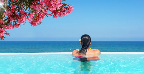 Woman relaxing in infinity outdoor swimming pool with sea ocean in travel vacation. Woman looking at the sea and resting in a flowery pool. - obrazy, fototapety, plakaty