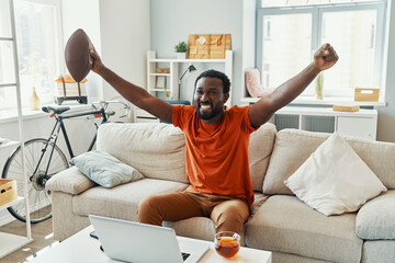 Excited young African man cheering and smiling while watching sport match at home