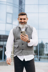 A bearded gray-haired senior man uses and talks on a smartphone