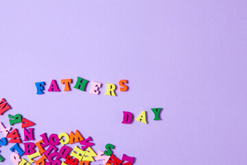 Fototapeta na wymiar Child's toy letters spelling Fathers Day next to randomly lying letters on purple background.
