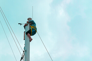 Sailor on top of sailing boat mast doing maintenance or radar system, mast harness human lifting...