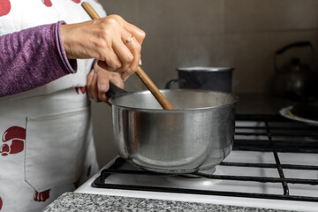 Woman cooking at home. Stirring a pot. Side view.