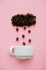 Coffee beans in shape of cloud pouring rain drops in a white cup on pink background.