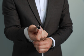 Stylish man holding cufflinks against grey background, closeup