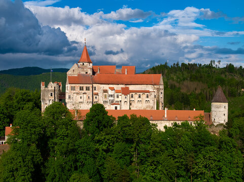Ancient royal Moravian castle Pernstejn, standing on a hill covered green forest against partly cloudy blue sky. Aerial photography.  Bohemian-Moravian Highlands, Czech landscape, travel point.