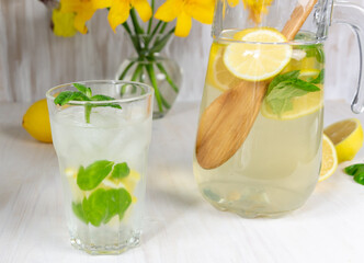 glass of lemon lemonade with mint and ice on white background, yellow lily, iris flowers in vase