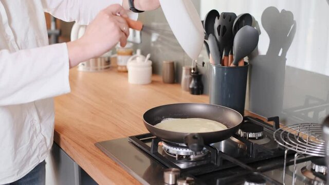 Closeup of woman hands cooking omelet, pouring eggs on frying pan on the kitchen. Whisk whip up eggs. Preparing breakfast at home
