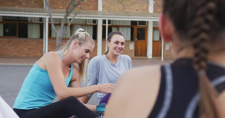 Diverse female basketball team sitting on ground and talking