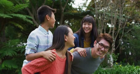 Smiling asian father and mother piggy backing happy son and daughter in garden