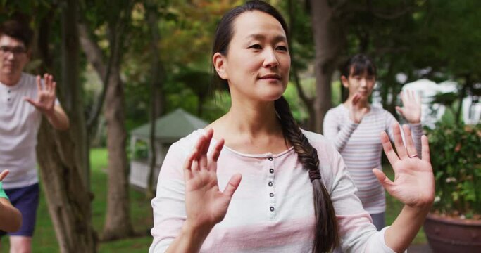 Happy asian parents exercising in garden with son and daughter, practicing tai chi together