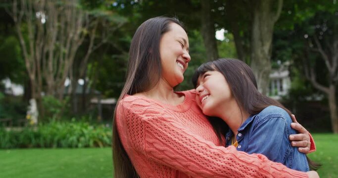 Smiling asian mother hugging happy daughter, having fun in garden together
