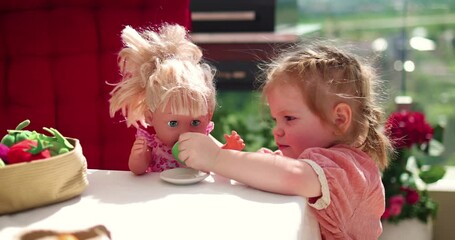 cute toddler baby girl treats a dolly with tea, role play game on summer terrace