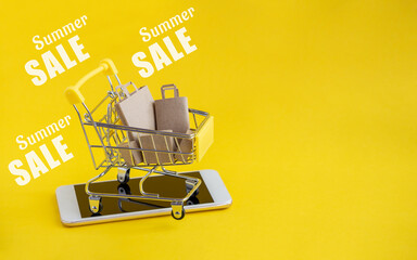 Metal cart with paper bags for goods, stands on cell phone. Text-summer sale is written on yellow...