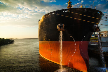 A large cargo ship is docked in the port of Catahena, Colombia at sunset and water flows from the...