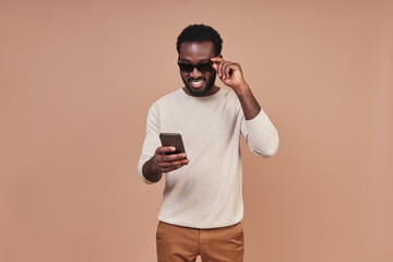 Handsome young African man in casual clothing using smart phone and smiling