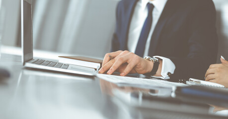 Unknown businessmen and woman sitting, using laptop computer and discussing questions at meeting in modern office, close-up