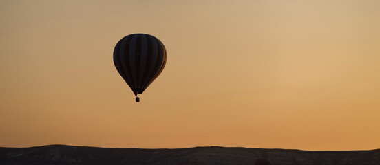 A hot air balloon flies over the horizon at sunset.