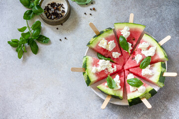 Fototapeta na wymiar Healthy seasonal dieting and nutrition, summer snack. Watermelon pizza with feta cheese and basil on a gray stone tabletop. Copy space.