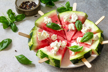 Healthy seasonal dieting and nutrition, summer snack. Watermelon pizza with feta cheese and basil on a gray stone tabletop.