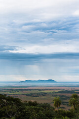 Beautiful view of the hills and open field in Paraguari, Paraguay, with the rain falling over the hills on the horizon and layers of clouds above them, trees in the foreground.