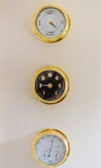 Brass tidal clock, moon phase clock and a barometer on a wall