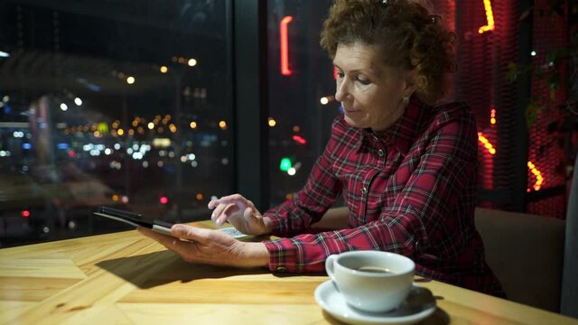 Senior woman using tablet in a cafe. Mature woman relaxing at a restaurant with tablet pc. Elderly female use digital tablet at coffee shop. Technology, old age and people concept. Mature student
