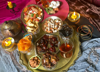 A table with Turkish tea with lale, oriental sweets, rahad delight, a mix of various nuts using copper dishes and bright fabrics.