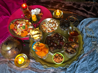 A table with Turkish tea with lale, oriental sweets, rahad delight, a mix of various nuts using copper dishes and bright fabrics.