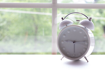 White analog alarm clock on table in front of window during day