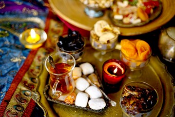 A table with Turkish tea with lale, oriental sweets, rahad delight, a mix of various nuts using copper dishes and bright fabrics.