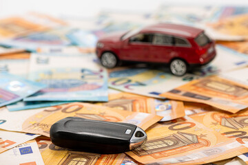 key and red toy car on pile of euro banknotes, buy or sell a car, rent a car or insurance concept